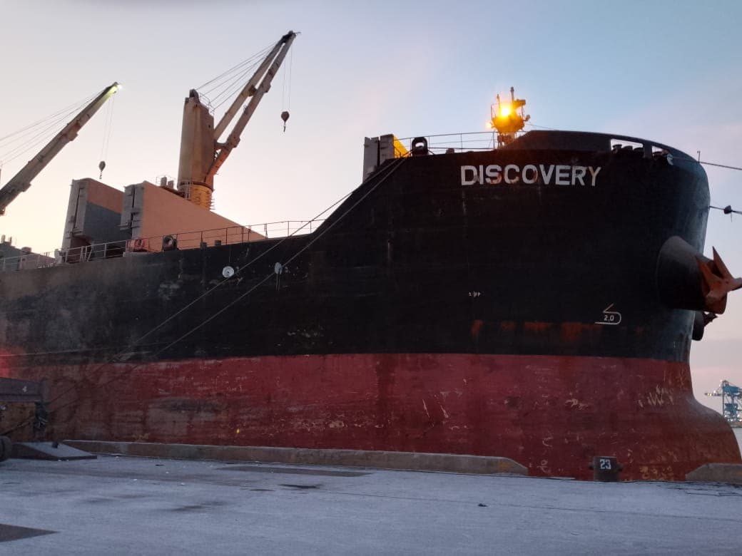 Bulk carrier berthed alongside the quay with deck cranes raised at dusk
