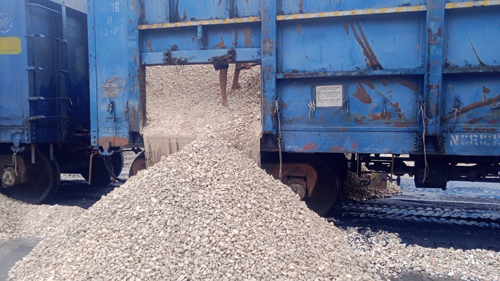 Crushed limestone pouring from an open railway wagon door onto a trackside heap