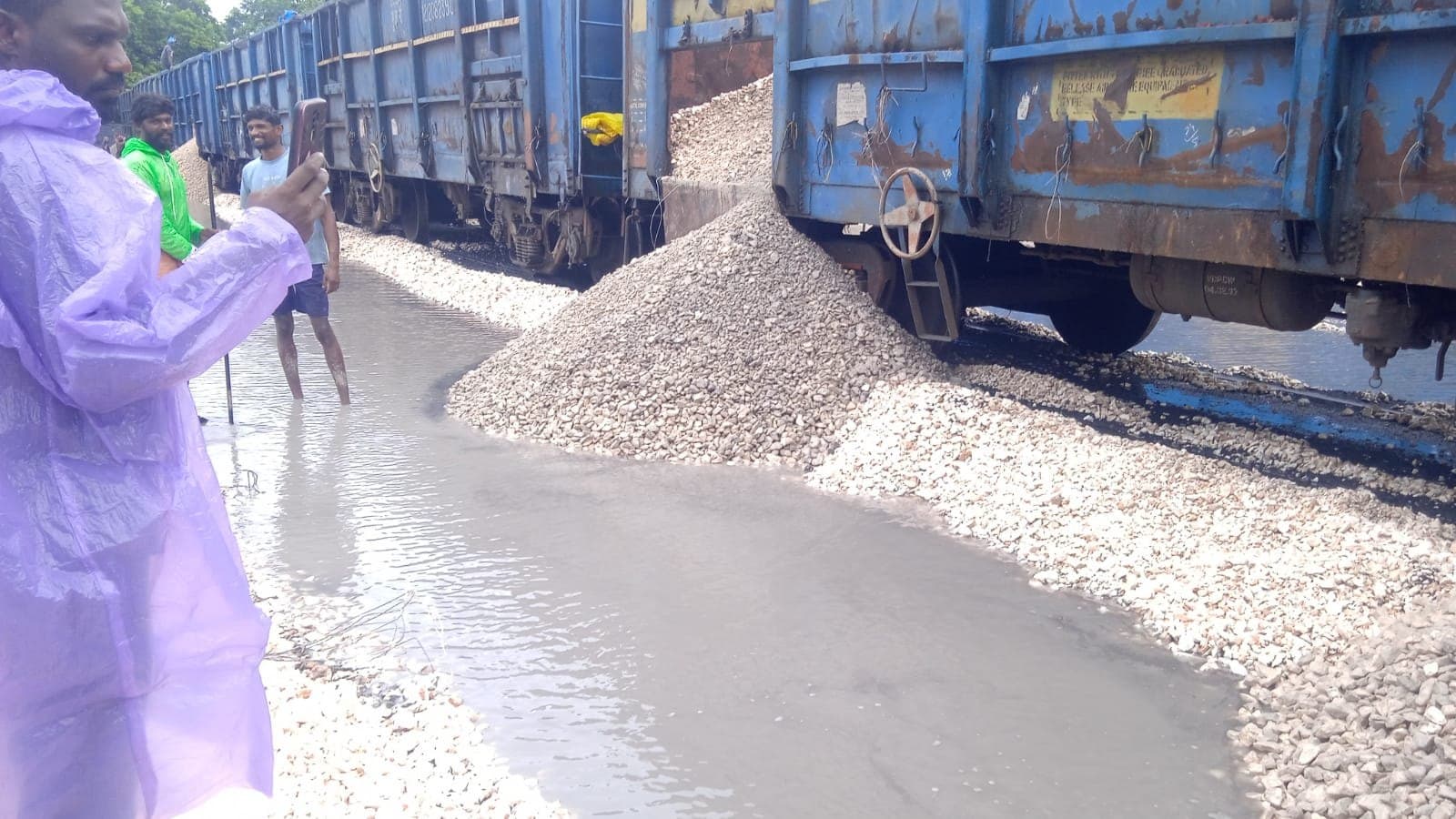 Workers in rain gear watching wagons unload aggregate at a wet railway siding