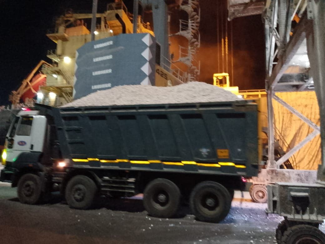 Loaded tipper truck carrying crushed stone past a port crane at night