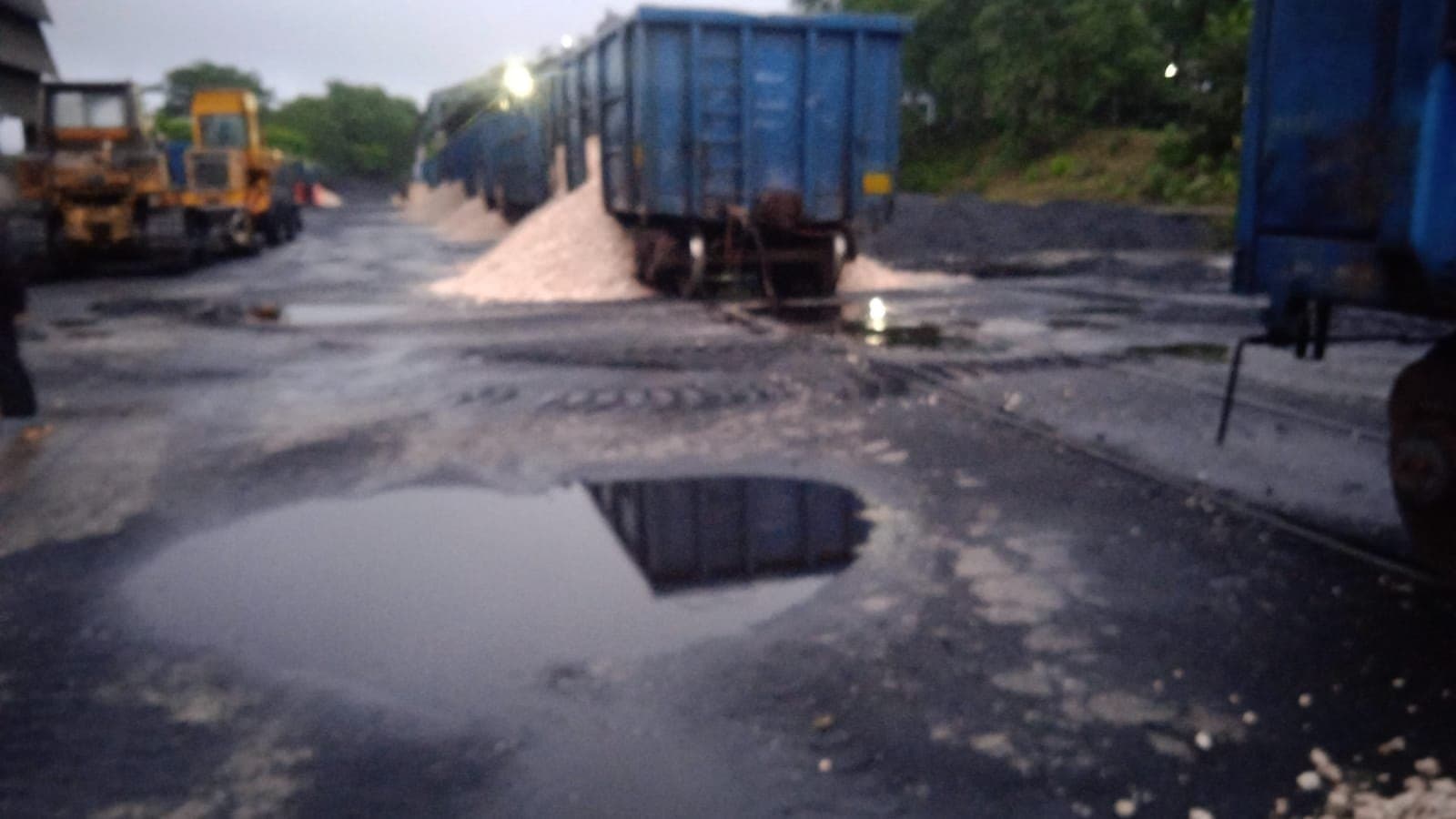 Rail wagons and a wheel loader at a siding with aggregate piles after rain