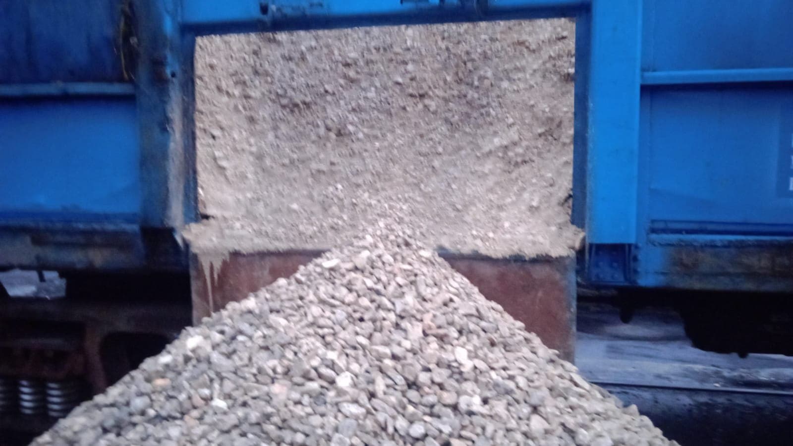 Close view of crushed stone spilling from an open wagon door onto a conical pile