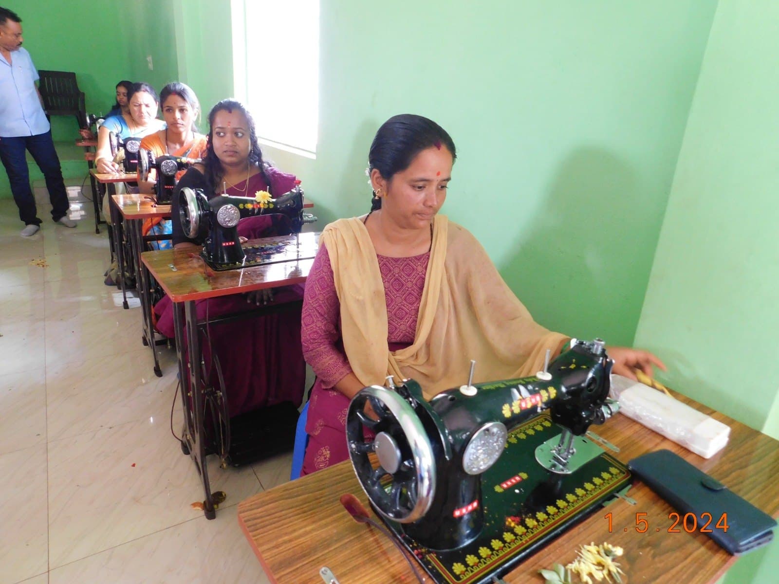 Trainee at a garlanded sewing machine during a newly opened tailoring centre session