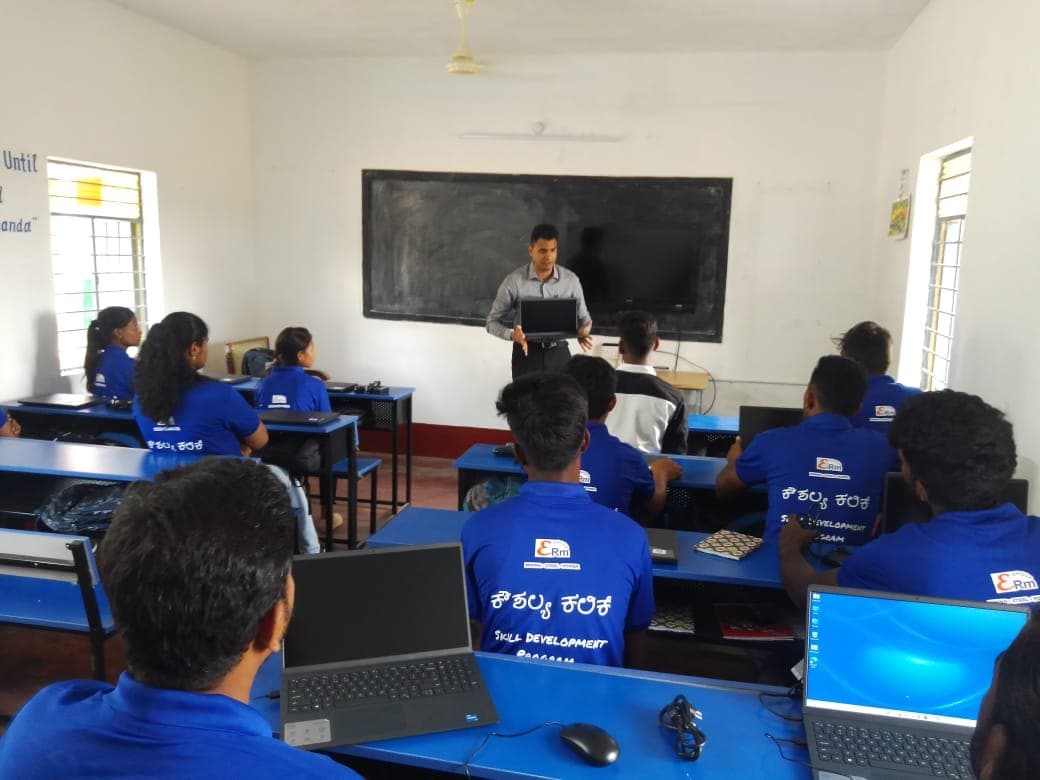 Trainer with a laptop addressing students in skill development T-shirts