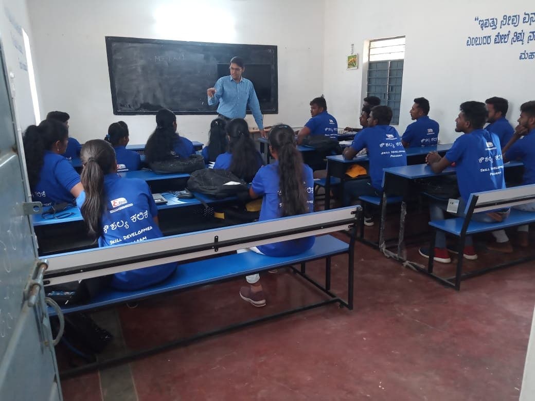 Trainees in blue skill development T-shirts listening to an instructor at the blackboard